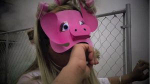 Anuj wearing a pink pig mask, biting his fist in front of a mesh fence.