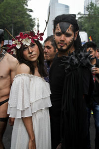 Two participants at Mexico City's Pride parade. One wears white and is made up to look like a fawn; the other dons all black and facial spikes.