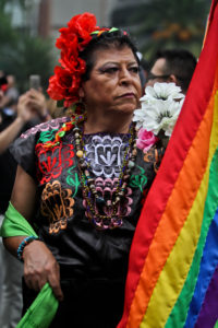 A particpant in the Mexico City Pride parade wears a colorful leather vest sporting cultural patterns and holds a rainbow flag.