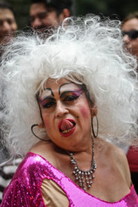 A close-up of the gender performer in exaggerated make-up and a white wig as they lick their lips.