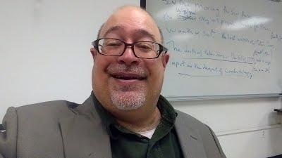 An image of Harry Hawk in front of a white board and a video screen.